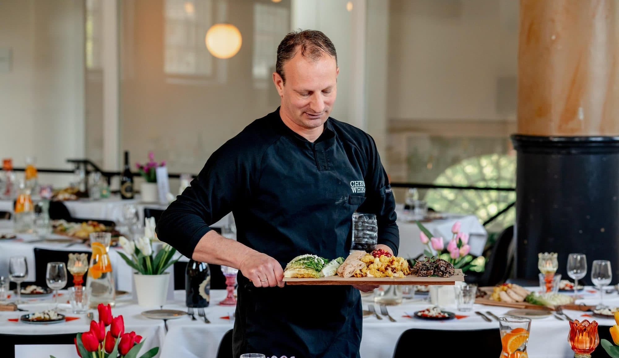 Chef Chanan carrying a board of dishes through a festively laid function room
