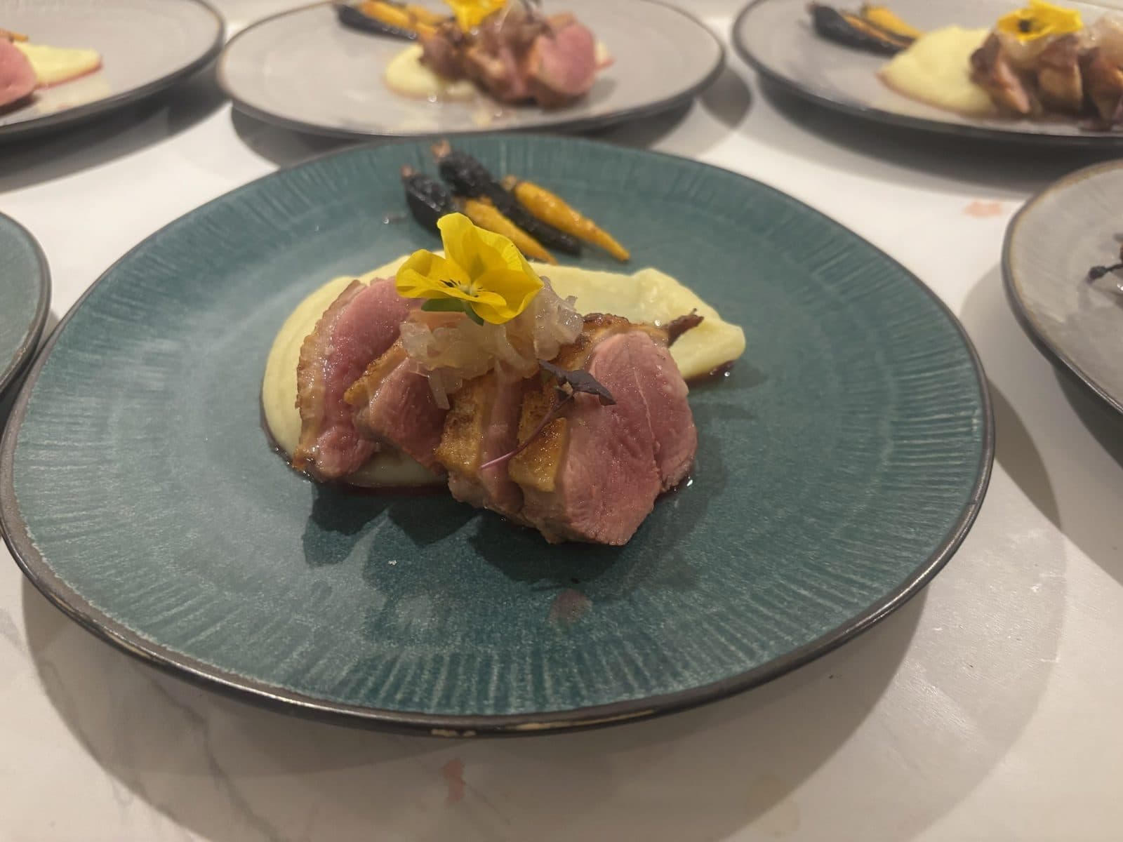 Gebakken vlees op puree met worteltjes en een gele eetbare bloem