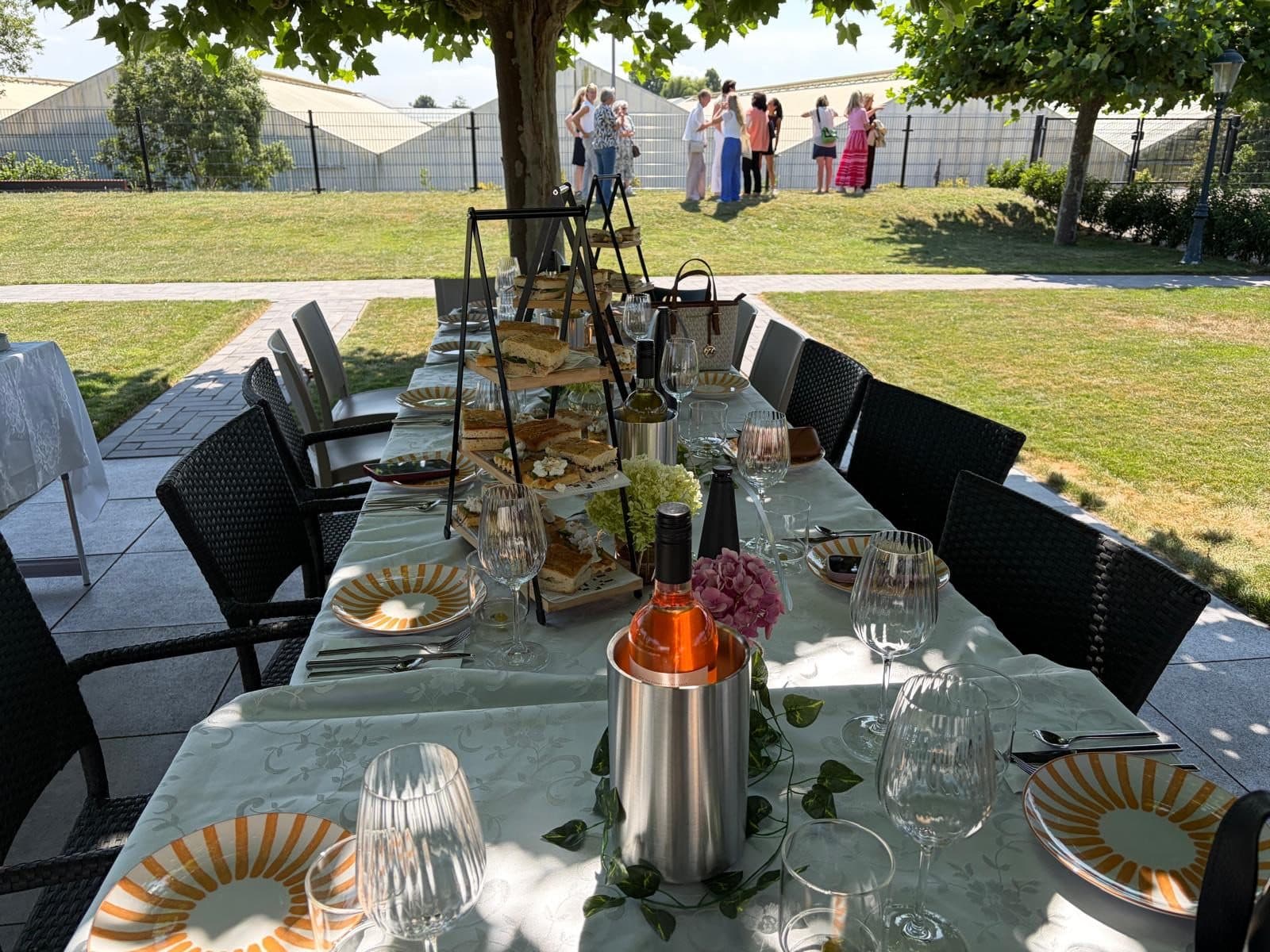 A long table laid outdoors under a tree, with bites, glasses and wine on ice